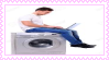 A man in casualwear sits atop a washing machine while browsing on a laptop.